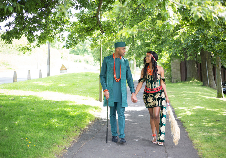 Bride and groom in traditional Nigerian clothing holding hands and smiling at each other while walking along path